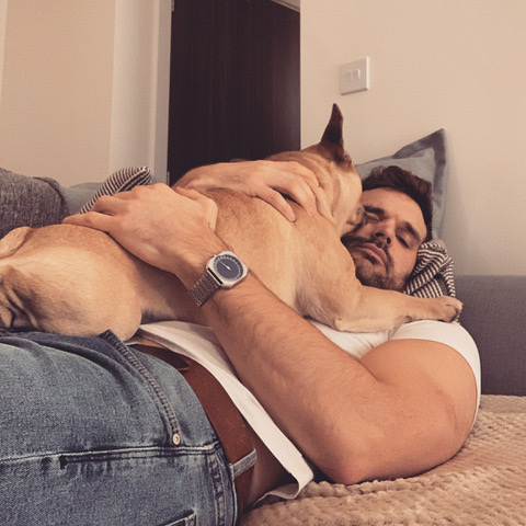 A man lies on a sofa with a large dog on his chest.