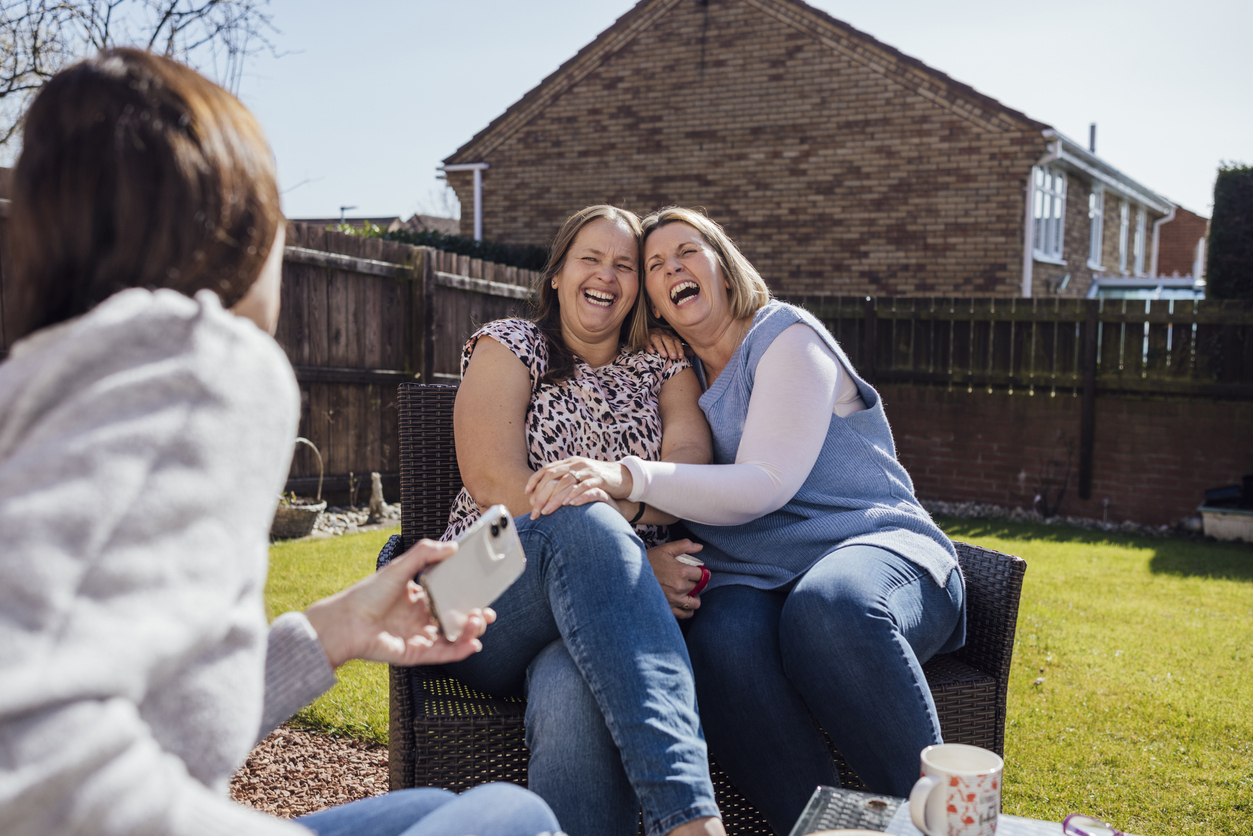 A group of women laugh and smile together as they drink tea in a sunny garden