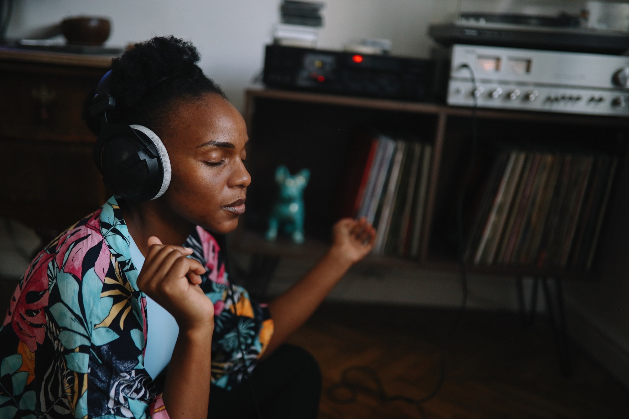A woman listens intently to music wearing large over-ear headphones while she sits on the floor in the room.