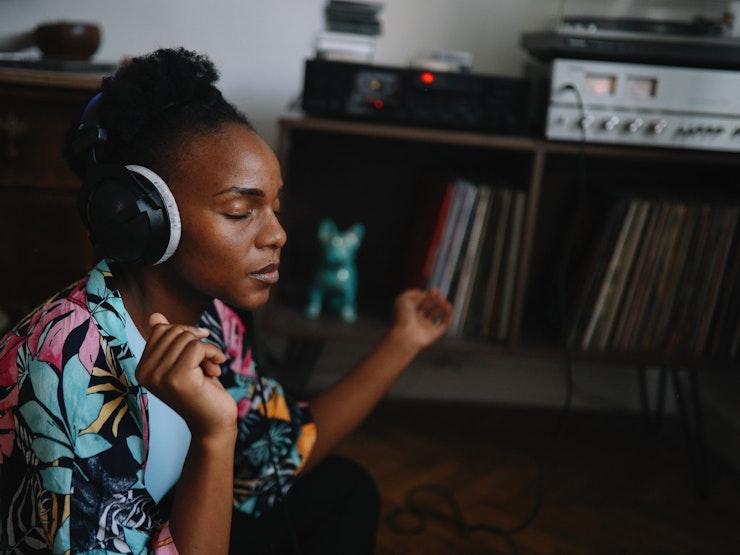 A woman listens intently to music wearing large over-ear headphones while she sits on the floor in the room.