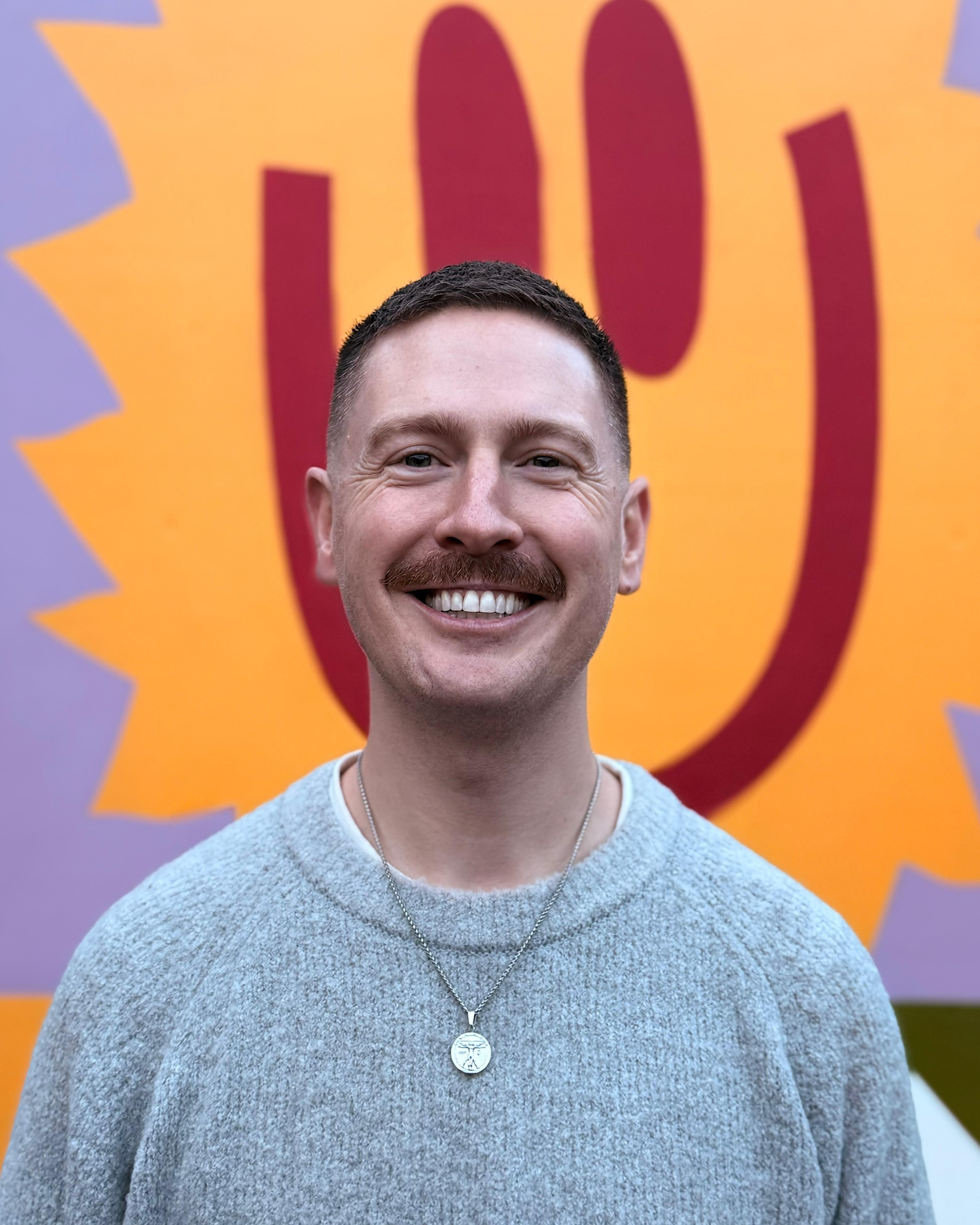 Karl smiling and looking directly at the camera in front of a colourful picture