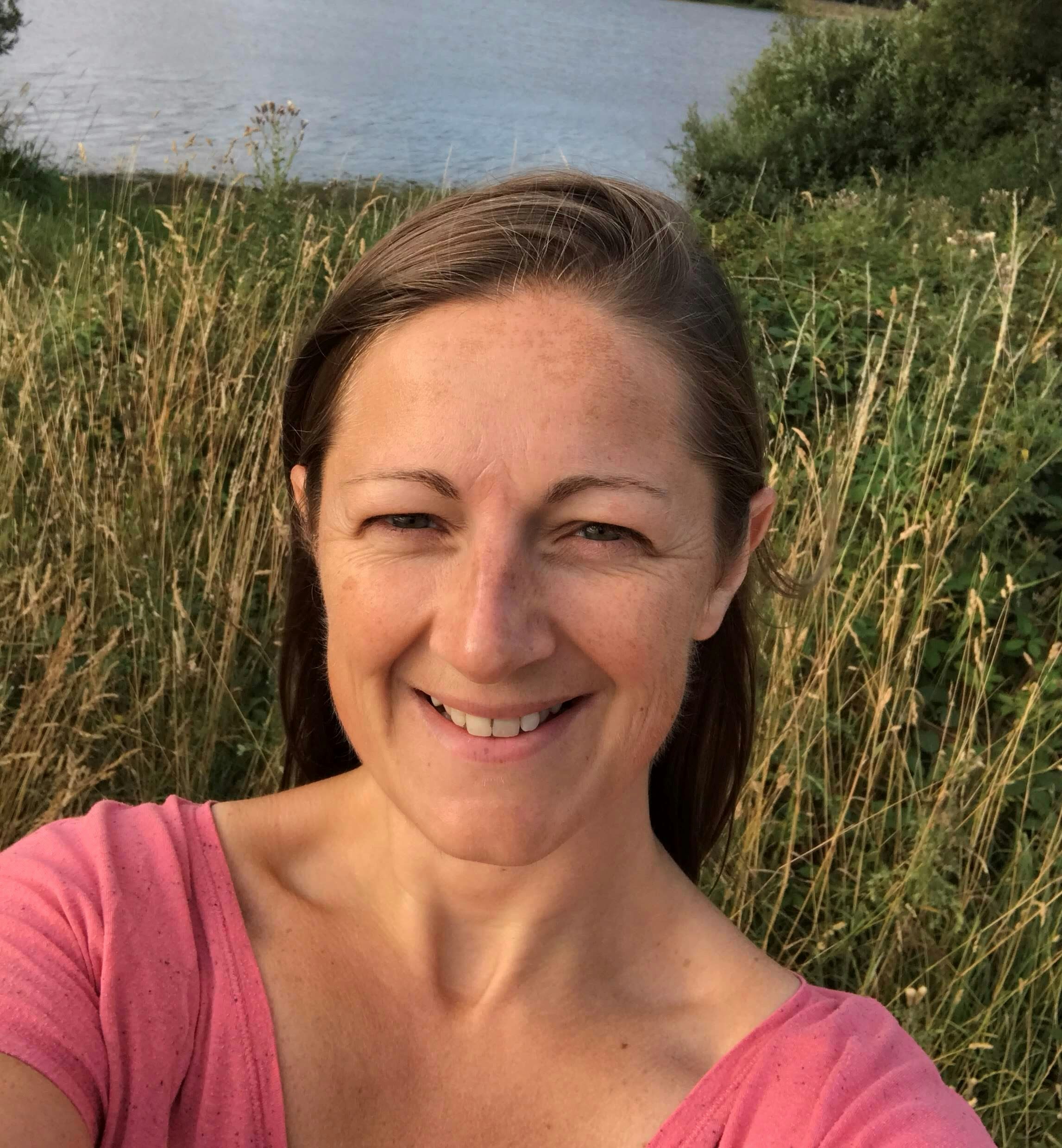 A woman with brown hair, tied up in a pony tail, smiles from an outdoor setting.