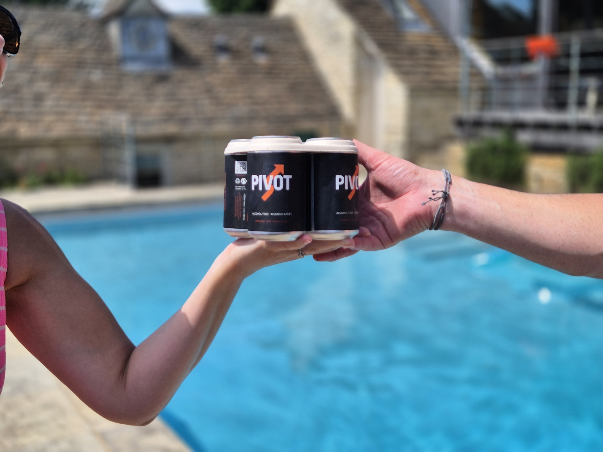 Close up of one person's hand passing a pack of drinks to another person by a swimming pool