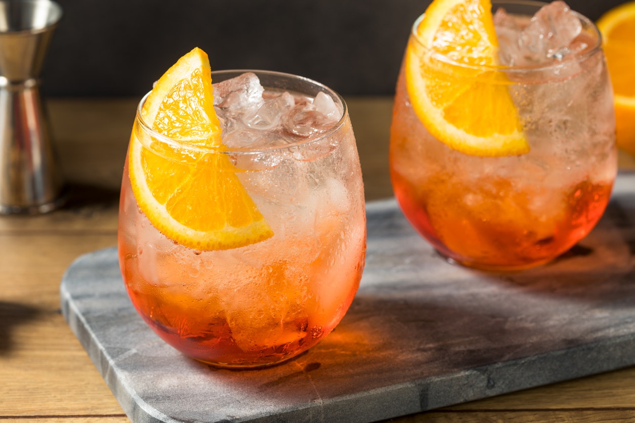 An icey orange drink garnished with a wedge of orange in a balloon glass