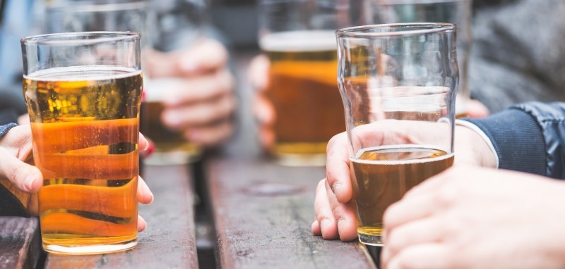 Three pint glasses on an outdoor table being held by hands.