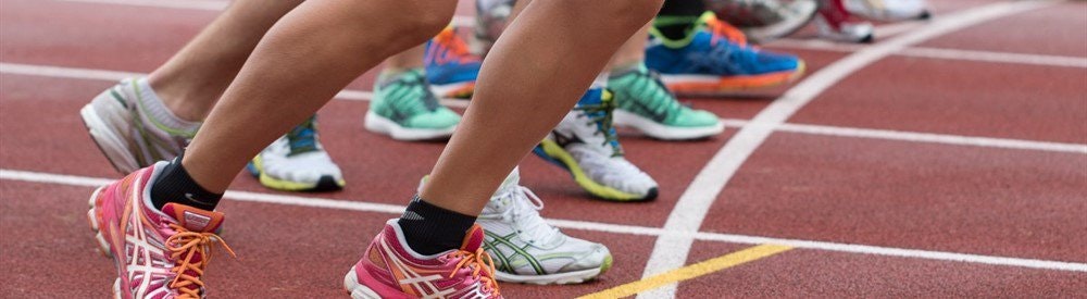 Runners' feet in colourful trainers line up along a painted start line.