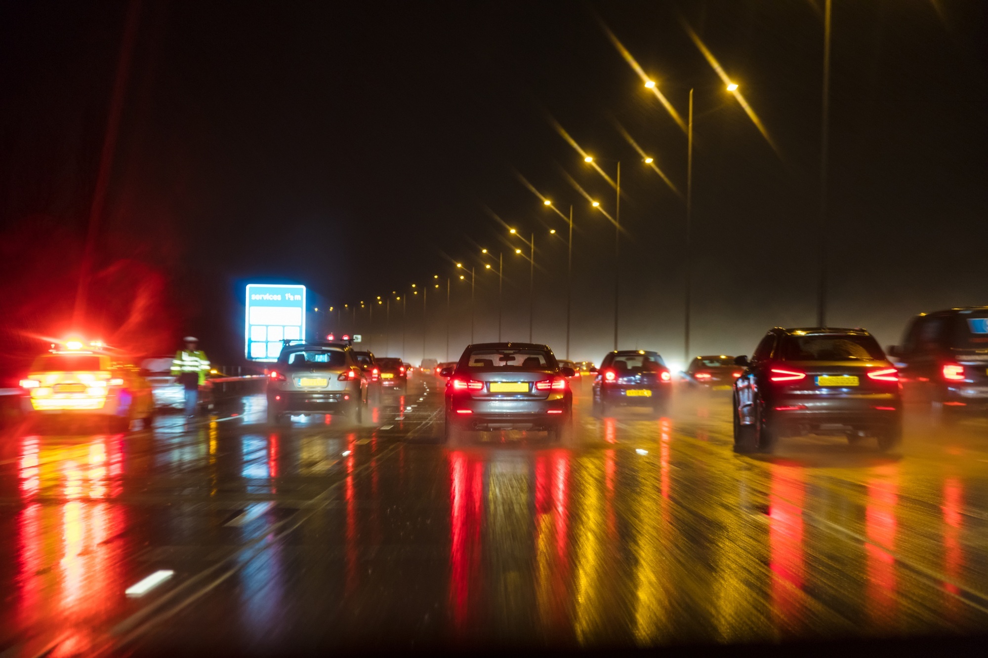 Blurred photograph of traffic at night in the rain on a motorway with police officer and car pulled over on the hard shoulder