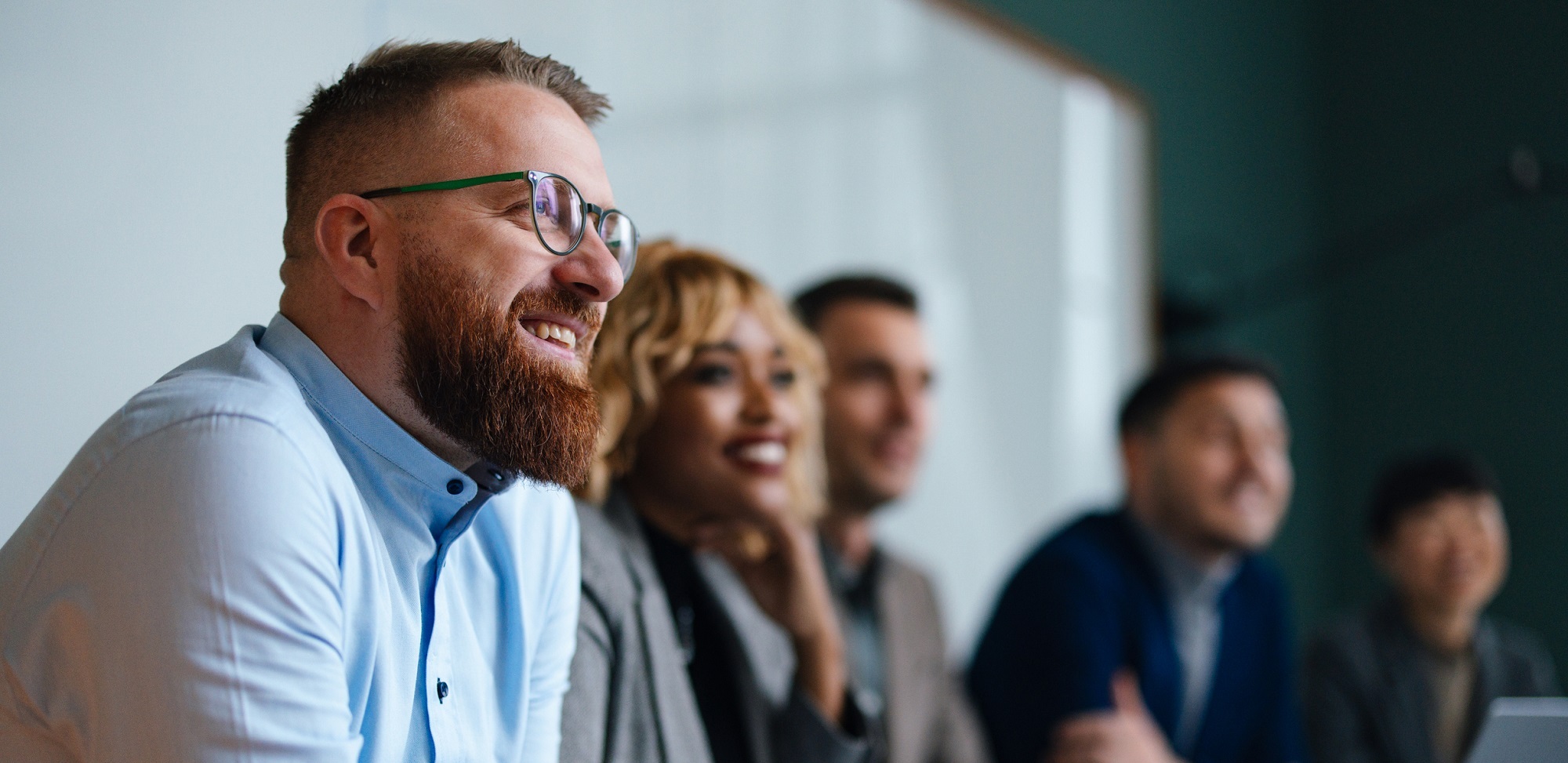 Smiling businessman and multi-ethnic group sitting in a row in a meeting room listening to a presentation