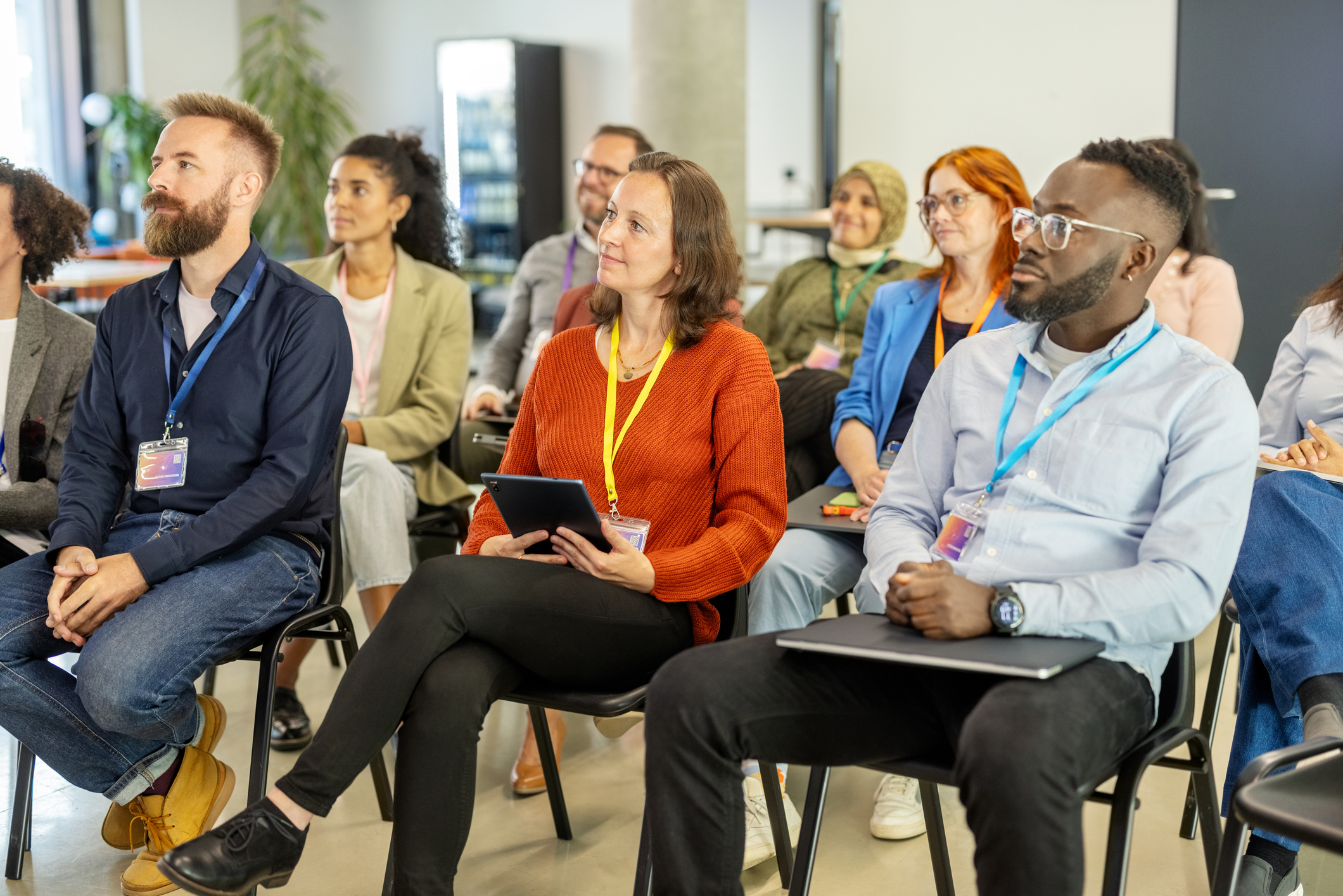 Business professionals from diverse backgrounds seated in rows listening to a speaker intently at a seminar.