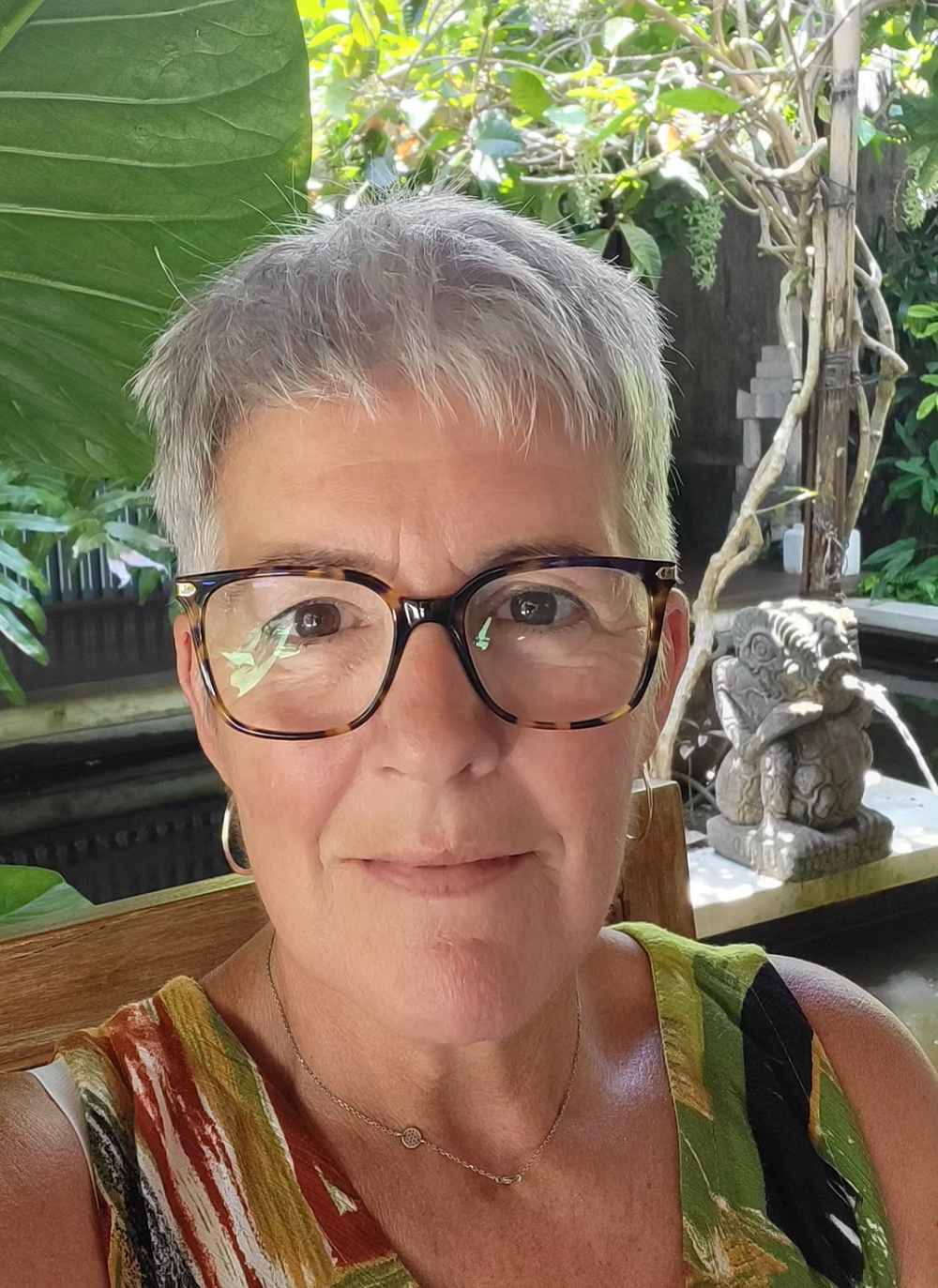 Carolyn smiles at the camera, with tropical plants pictured in the background.