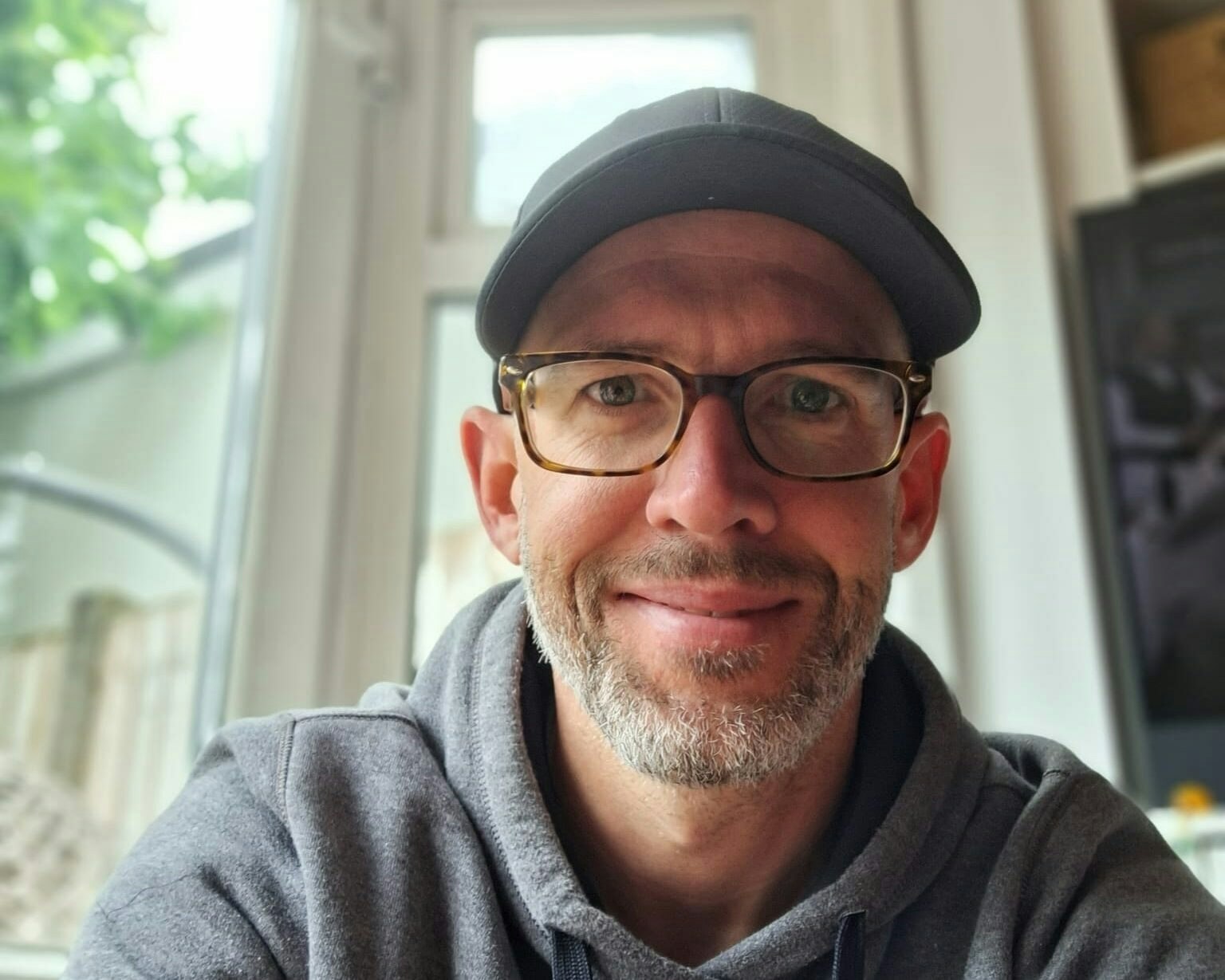 Patrick sitting at a desk with a hat on smiling at the camera