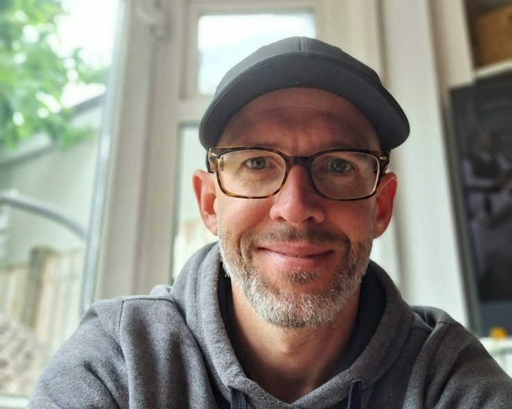 Patrick sitting at a desk with a hat on smiling at the camera