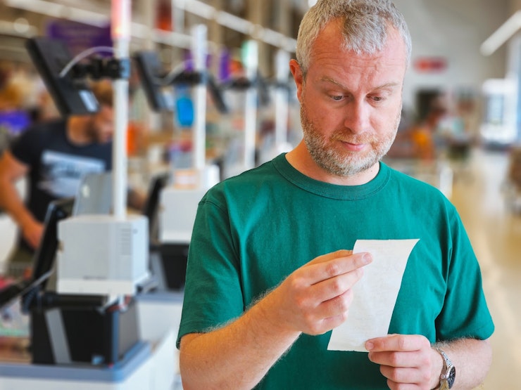 Close up of a man checking receipt in the supermarket after making purchases at checkout