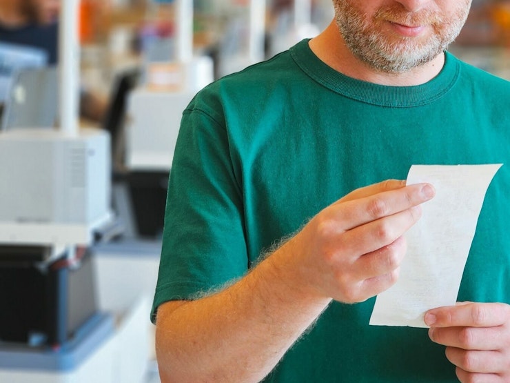 Close up of a man checking receipt in the supermarket after making purchases at checkout