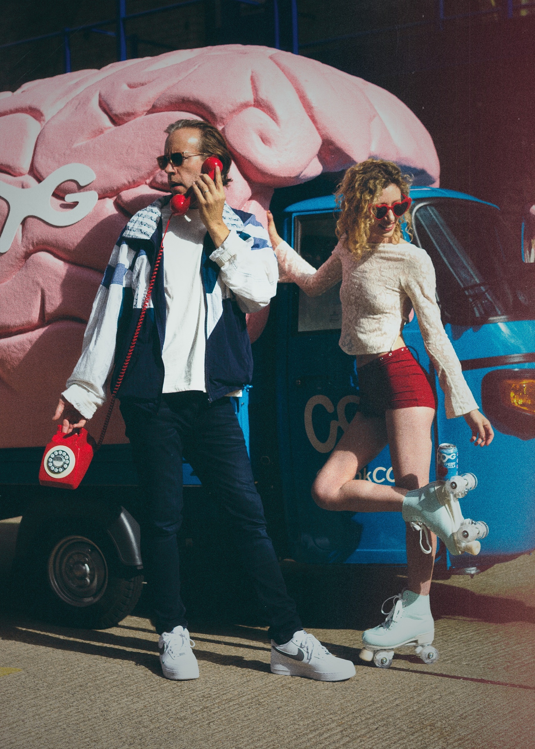 Two people standing against COG brain van one using a phone prop the other in roller boots.
