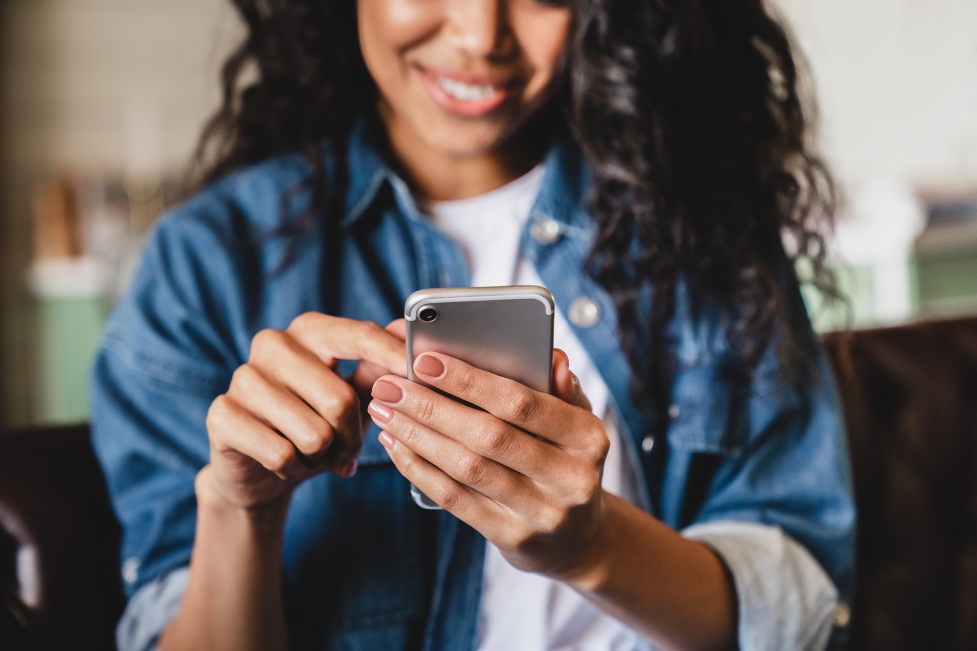 Cropped shot of a young woman using her smartphone at home sitting on a sofa