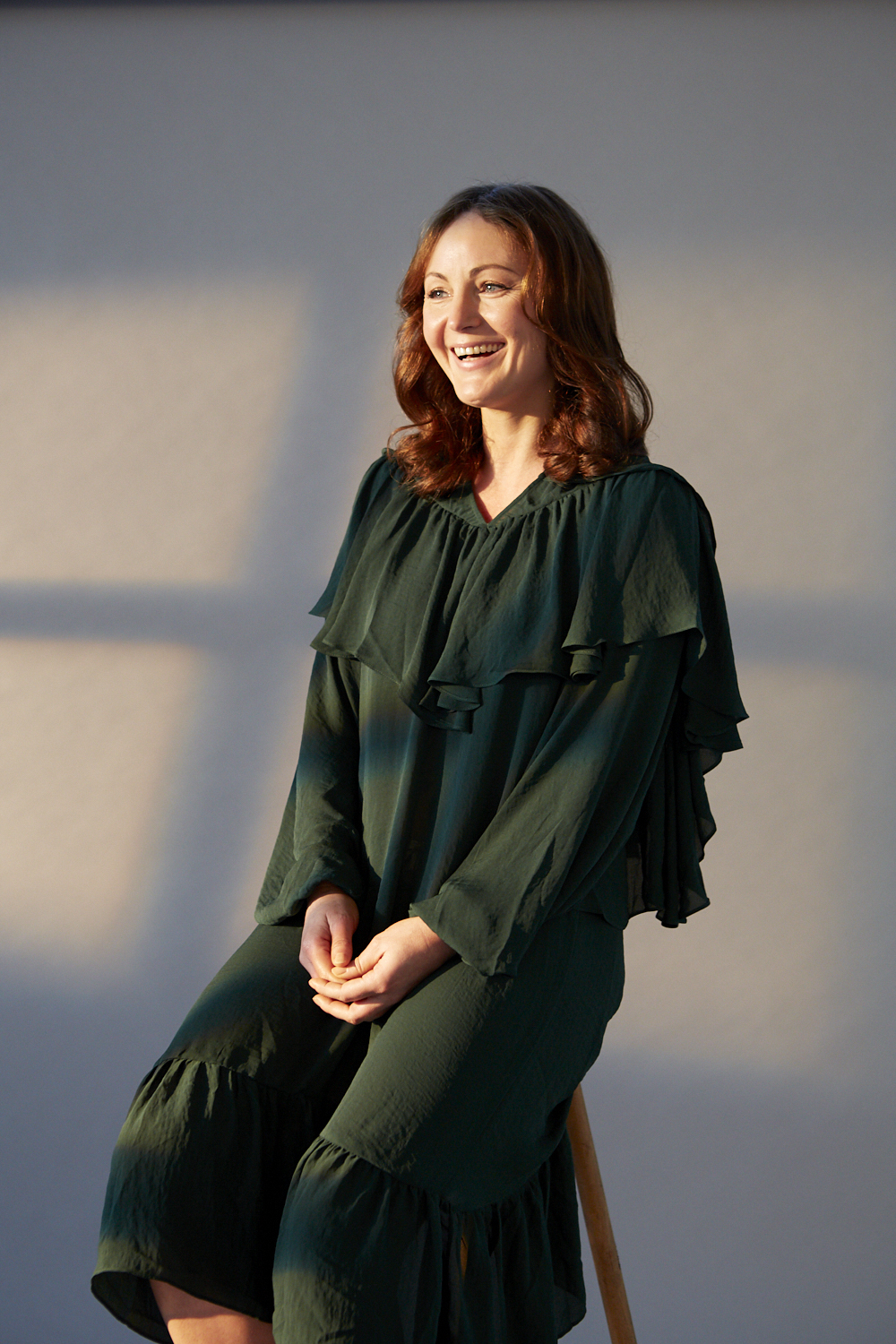 A woman in a black dress sits on a stool, smiling.