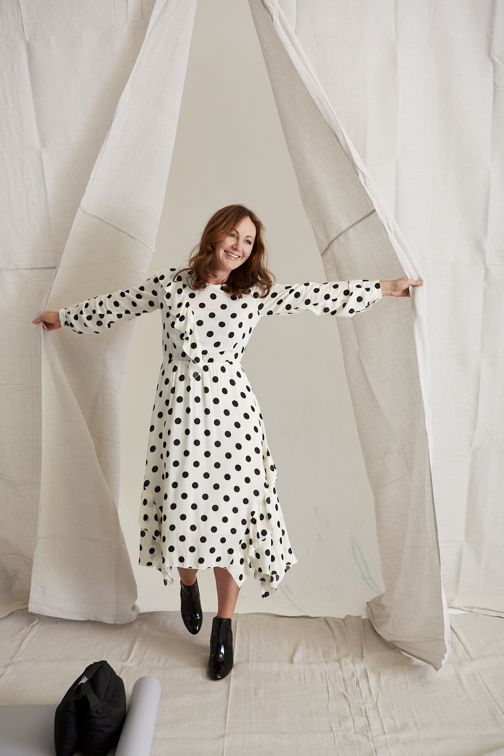 A woman in a polka dot dress bursts through a pair of white curtains.