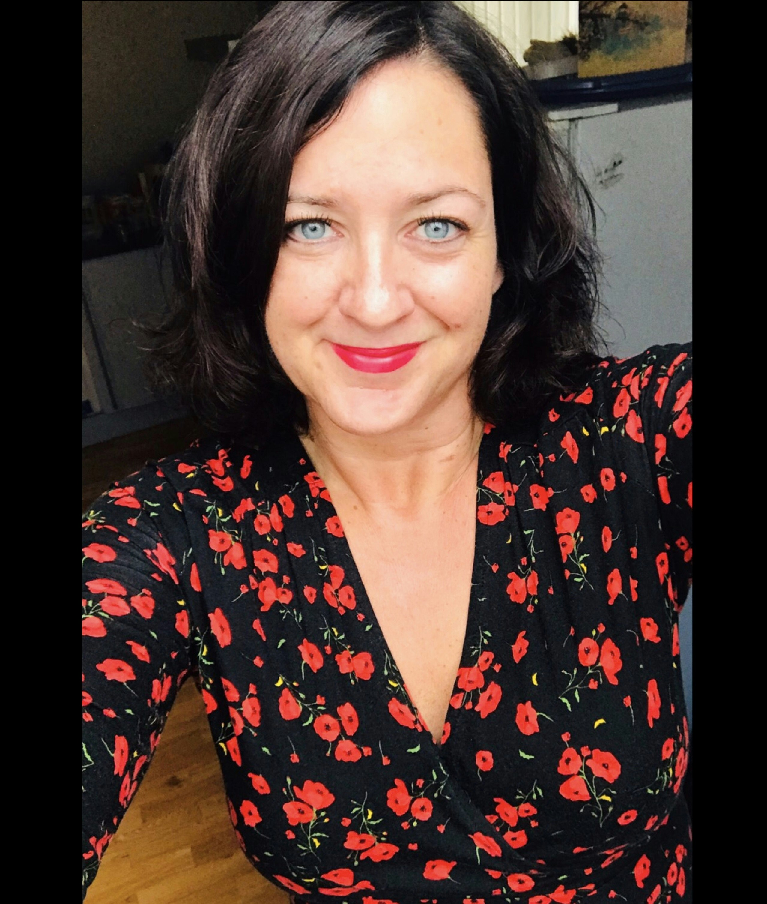 An older woman with black hair wearing a red floral dress smiles.