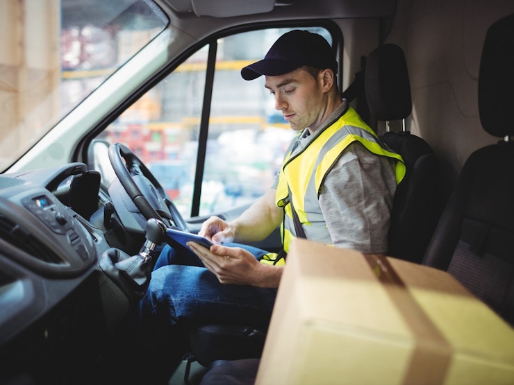 Delivery driver using tablet in van with parcels on seat