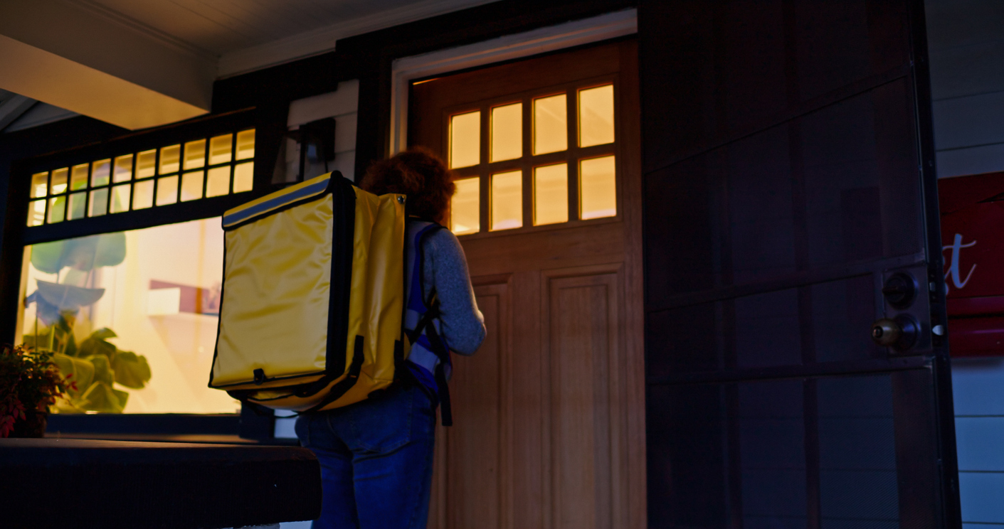 A delivery person walking up to a door to deliver a package at night time