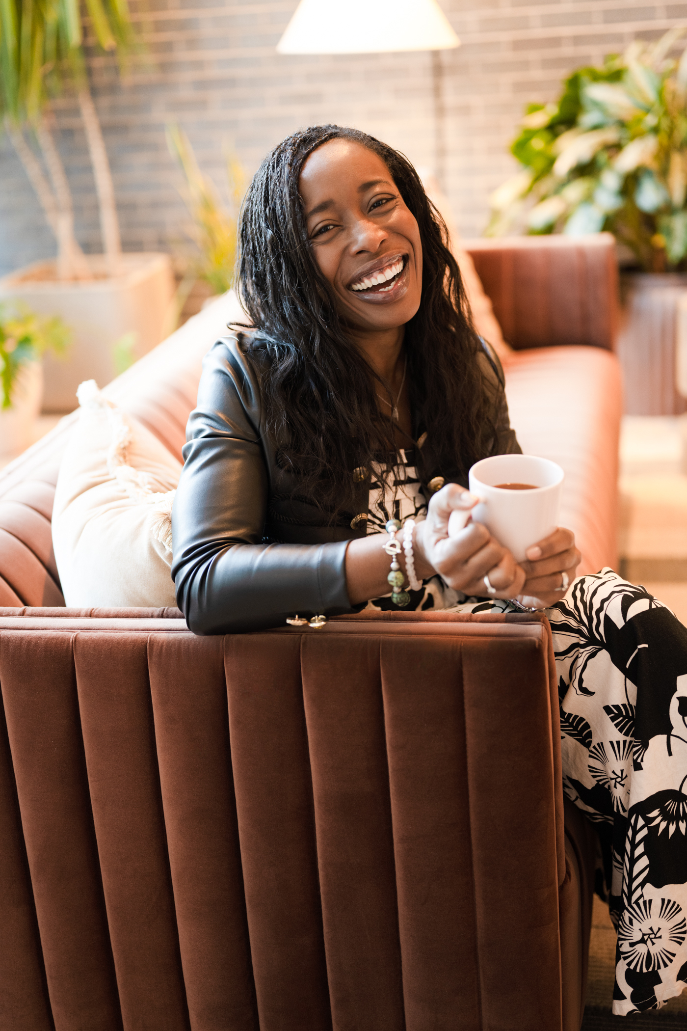 A woman sitting in a cafe smiles as she holds a cup of tea.