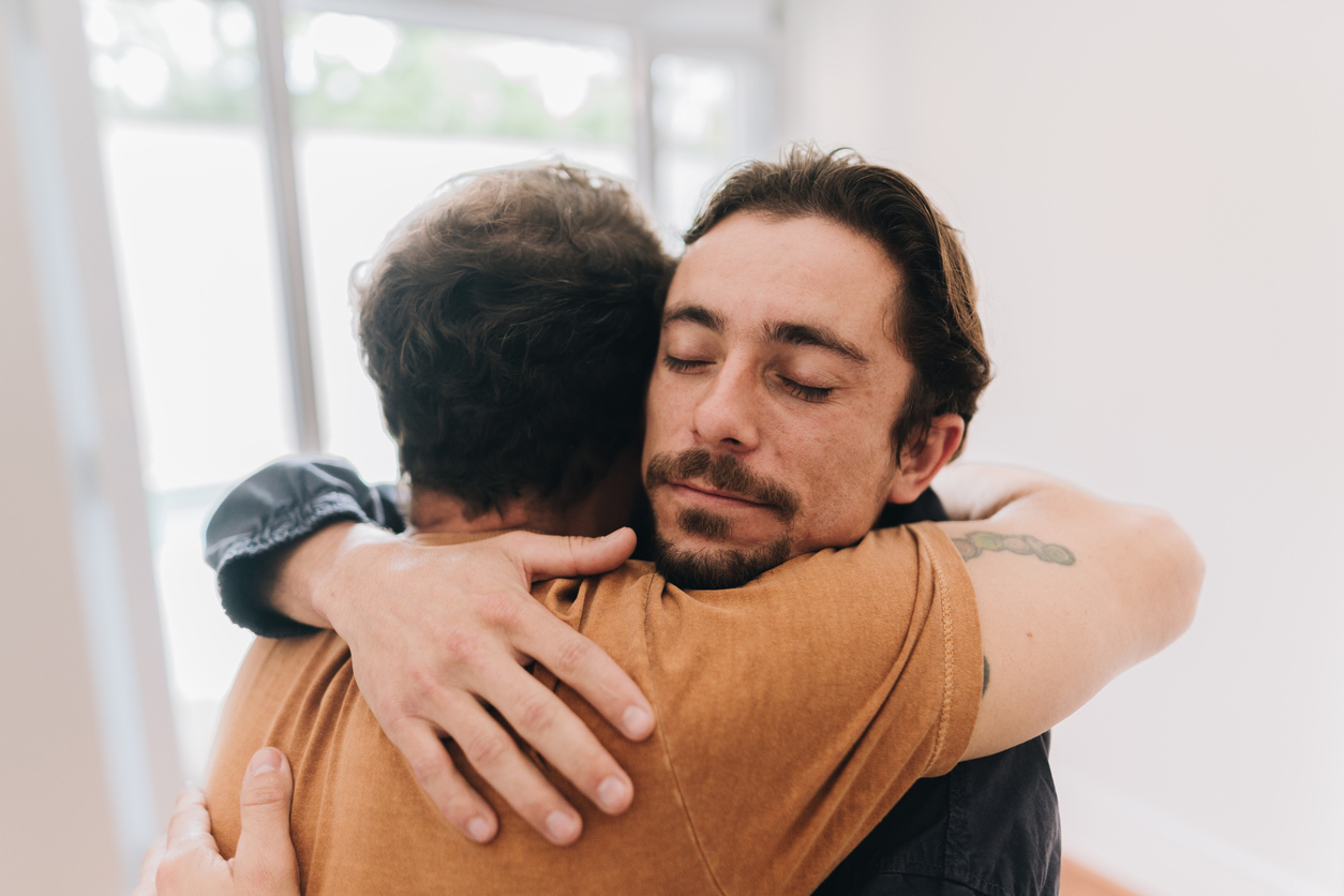 A father and son embracing while standing by a window at home
