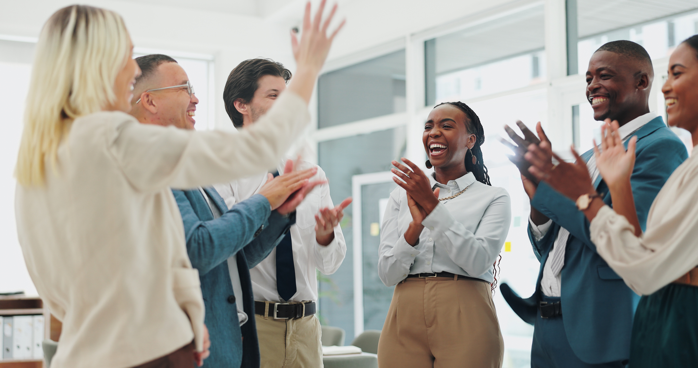 Group of employees standing in circle, smiling and clapping for collaboration, teamwork at workplace