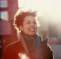 Happy urban women in her 30s walking outside on a chilly day with the sun behind her