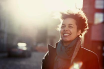 A woman wearing a wooly scarf and coat smiles on a city street.