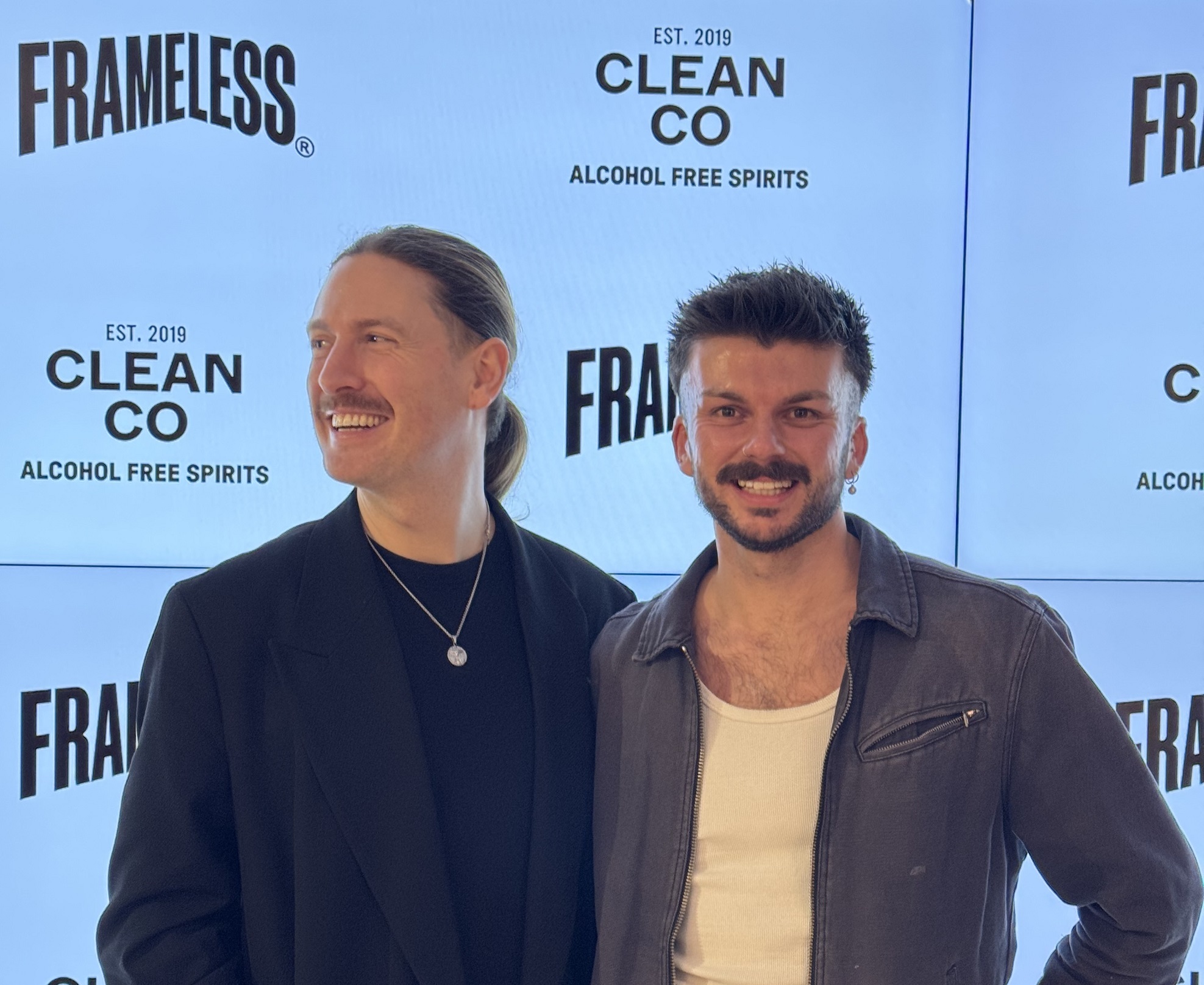 Two men side by side smile and laugh while posing for a camera.