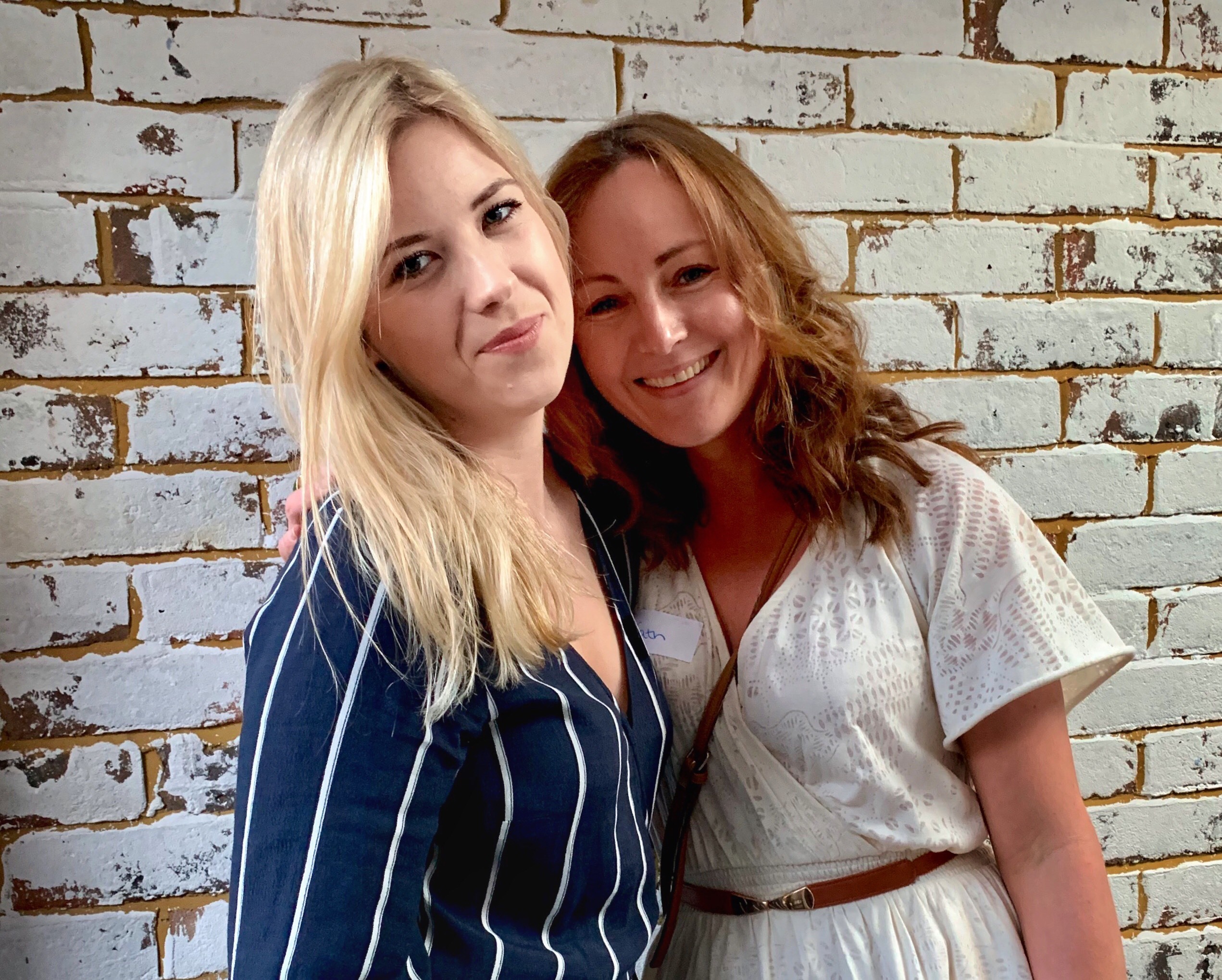 A blonde woman and a brunette woman embrace.