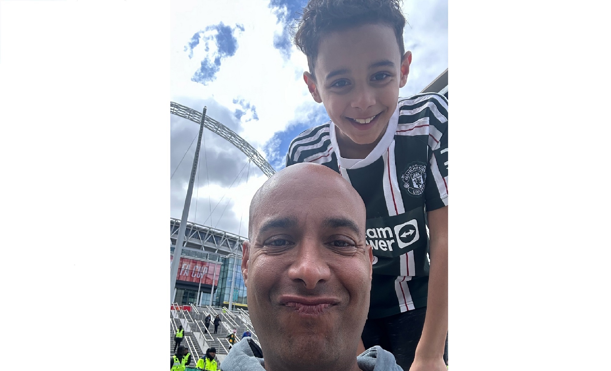 A man with a boy on his shoulders wearing a football shirt stand outside a football stadium.