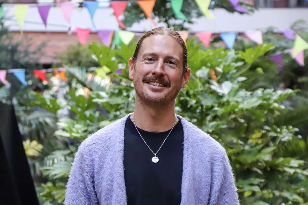 A man standing in a garden with colourful bunting behind him smiles at the camera.