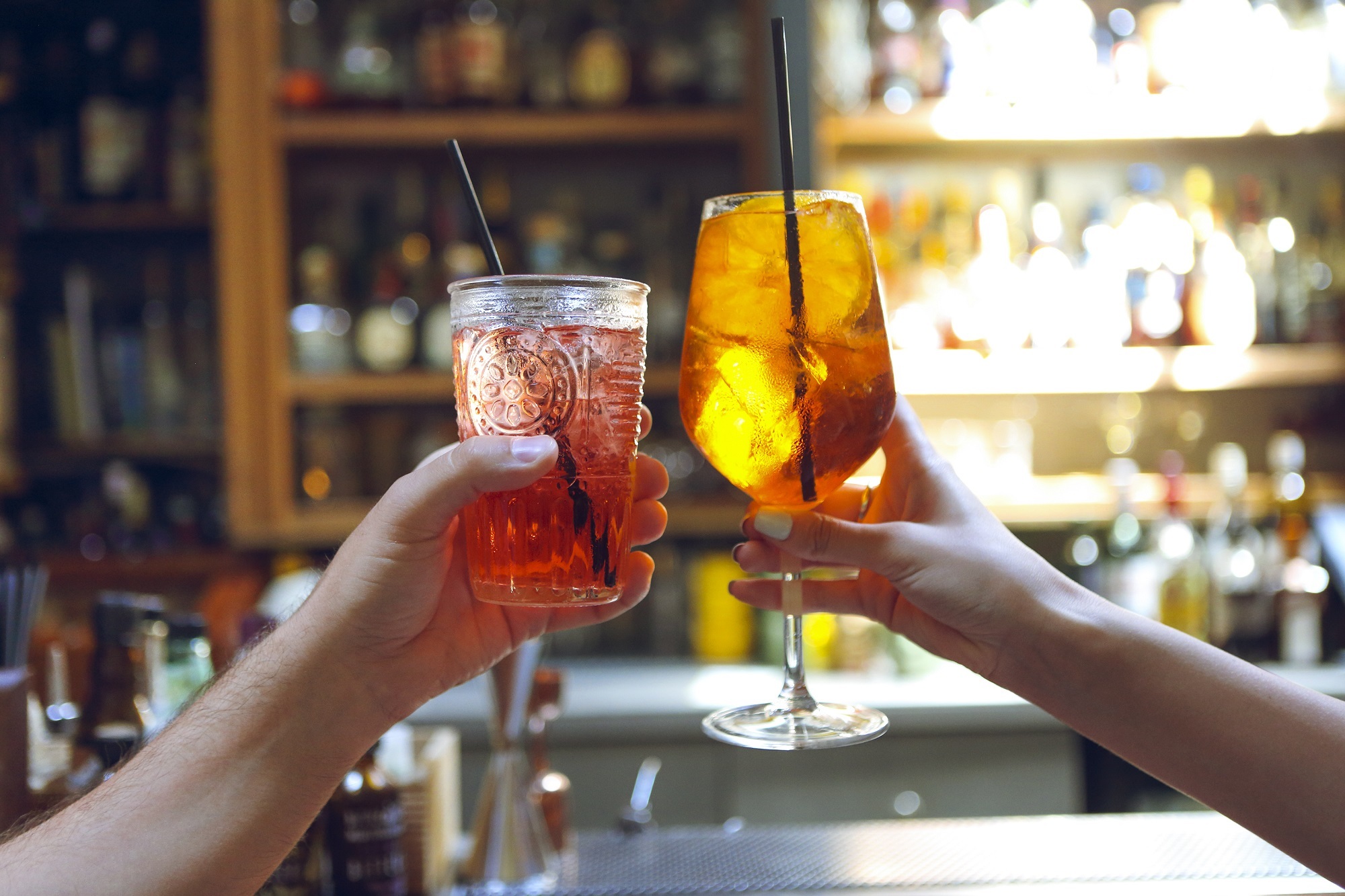 Woman and man raising glasses of cocktails in a bar background.