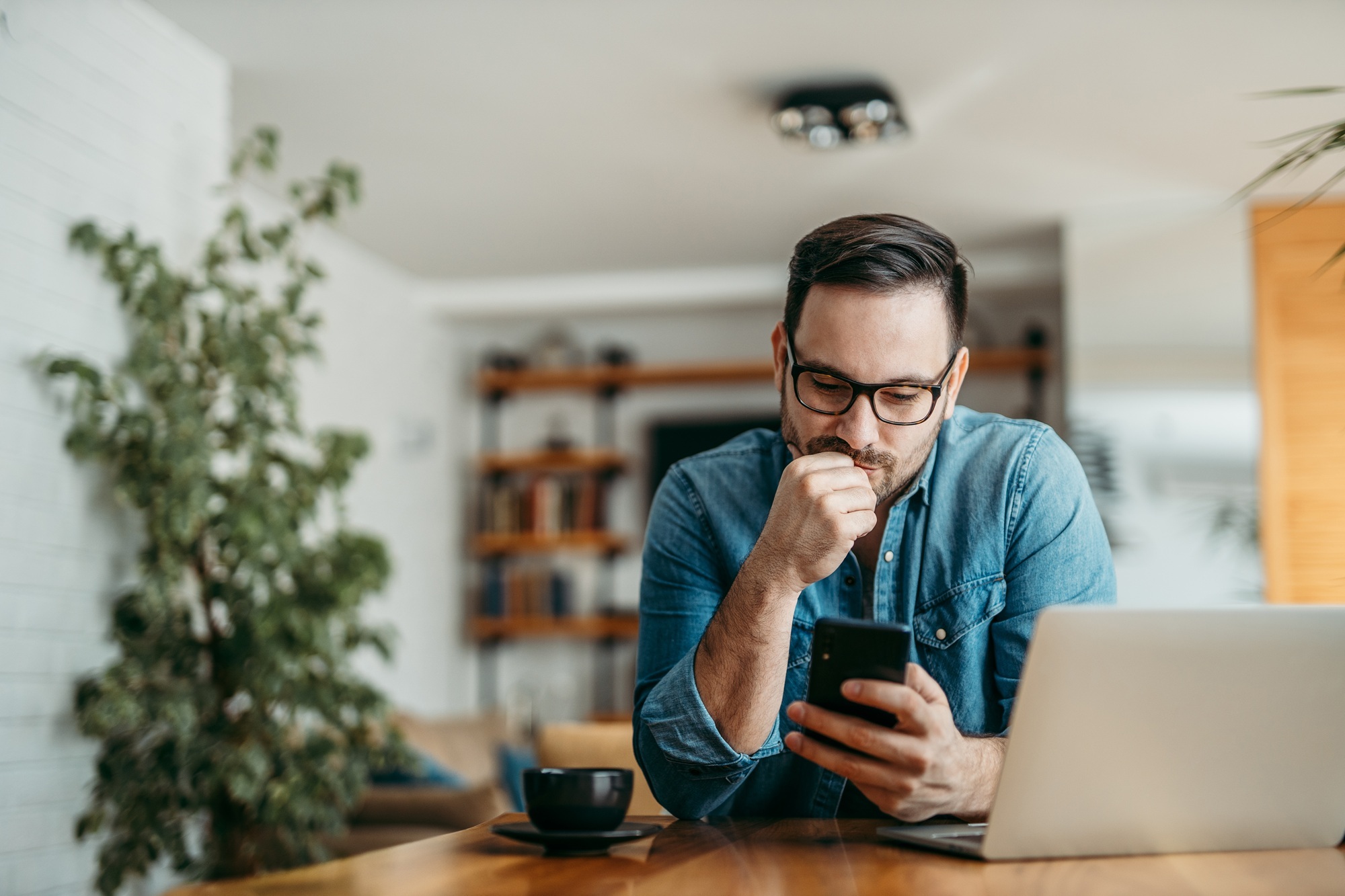 Portrait of a man looking intently at his smart phone, sitting at table at home