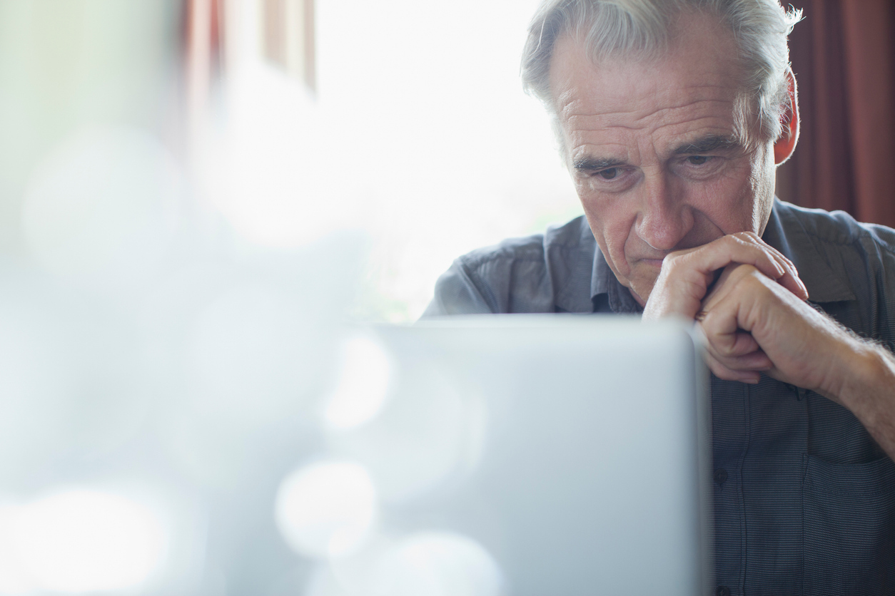 Man with hands clasped reading from laptop at home