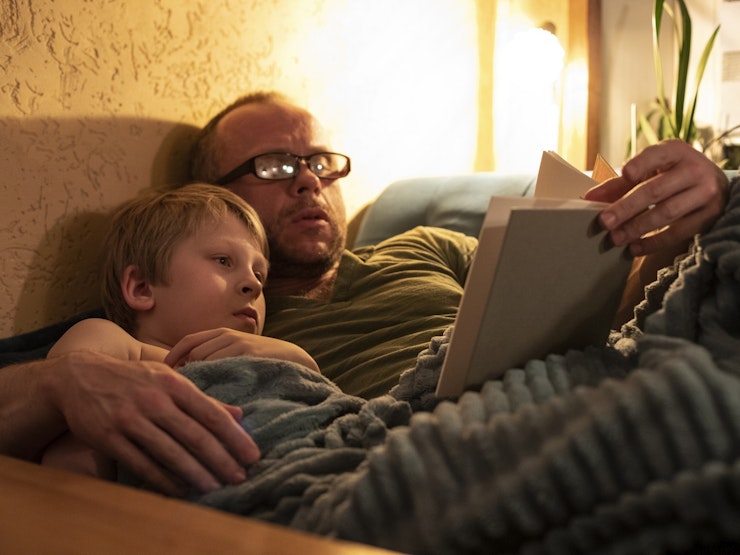 Man wearing glasses reads a child story by bedside light i Stock 1400806778 2 K px