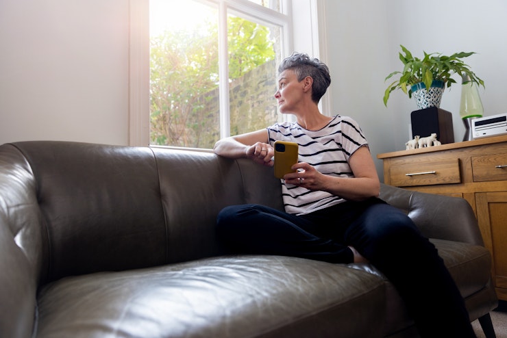 Mature woman sitting on sofa at home looking out of her window