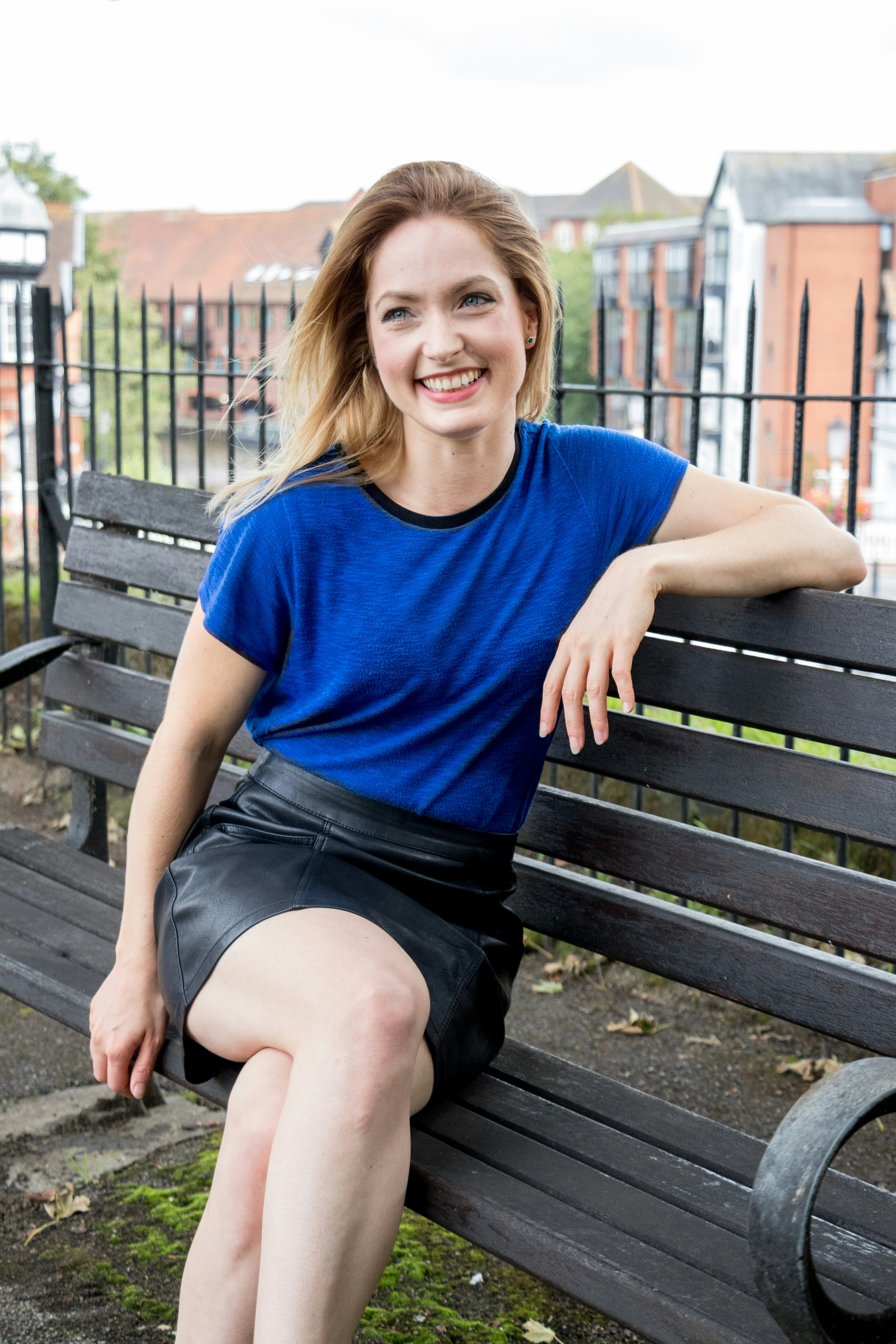 A young woman sits on a city park bench and smiles.