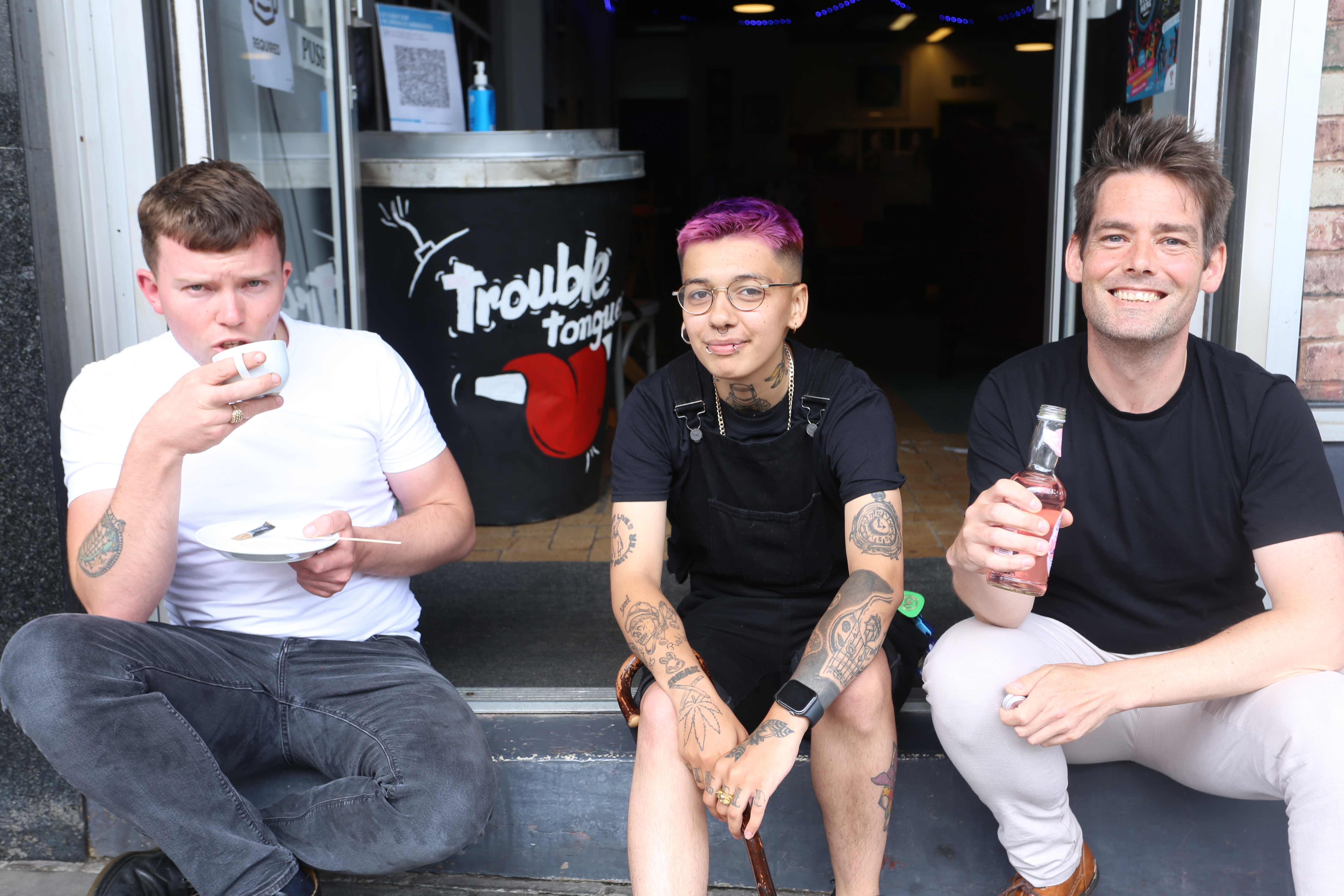 Three people sit on a step outside the cafe, drinking alcohol-free drinks.