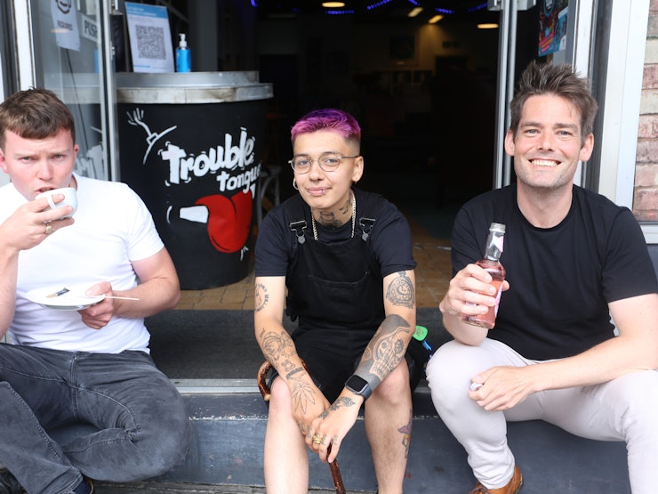 Three people sit on a step outside the cafe, drinking alcohol-free drinks.