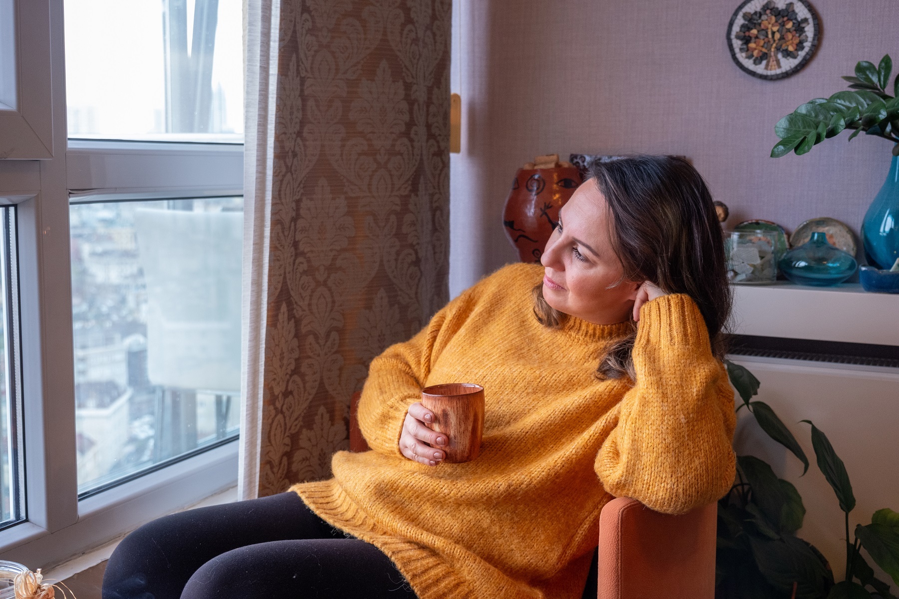 Middle aged woman wearing a yellow jumper looks pesively out of teh window whilst holding a cup i Stock 1927876833 under 2 K px