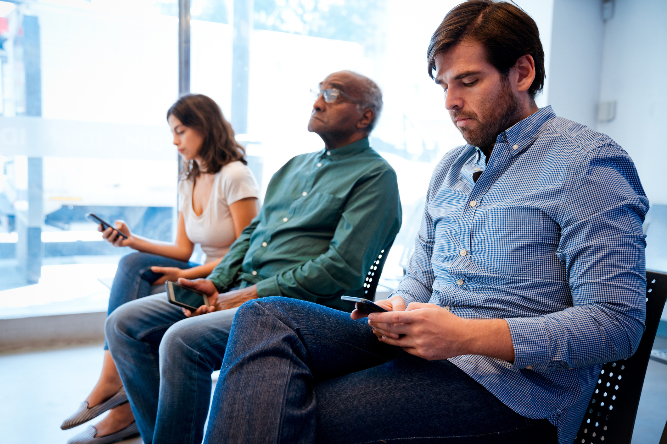 Three patients using smart phones sitting in health centre waiting room