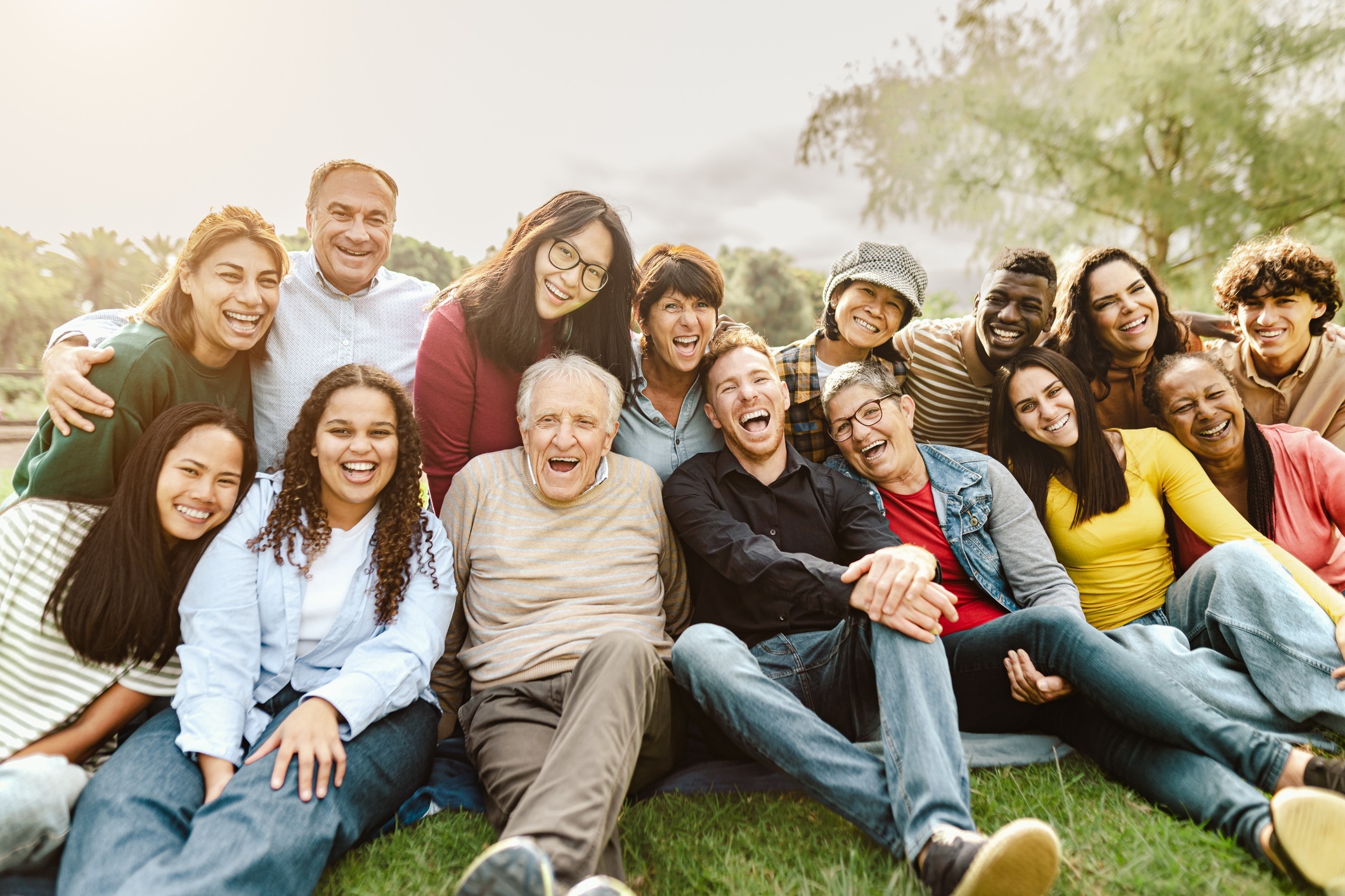 Multi generational diverse group having fun sitting on grass in local park