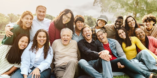 Multi generational diverse group having fun sitting on grass in local park