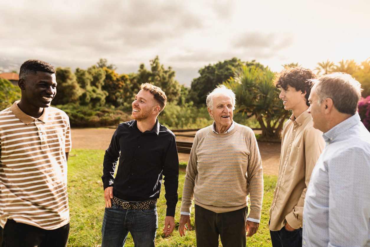Happy multigenerational group of men with different ethnicities standing up talking together in a public park