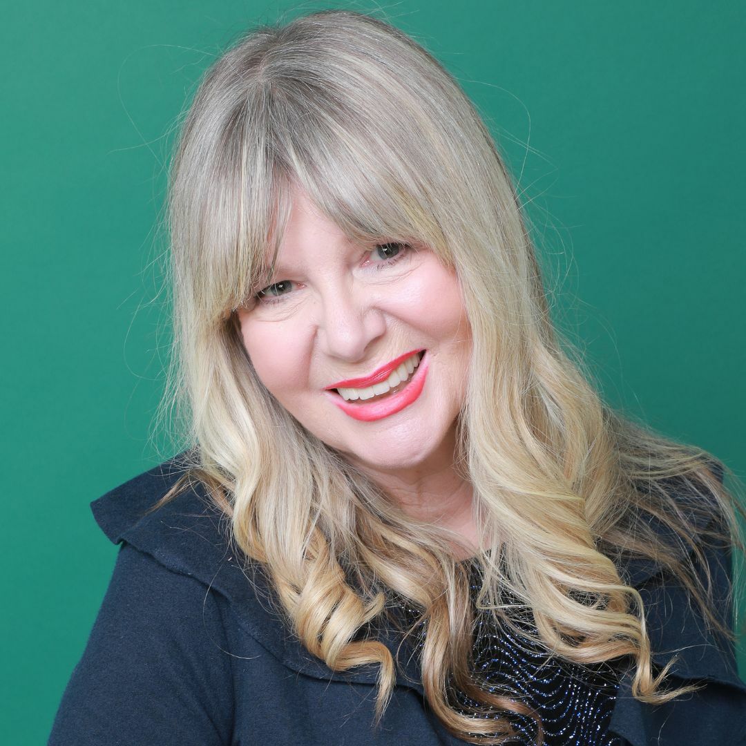 A woman with long, blond wavy hair smiles broadly at the camera from a green background.
