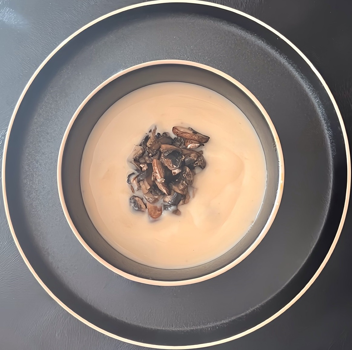 A bowl of French brie soup with sliced mushrooms on top with non-alcoholic brandy cream.