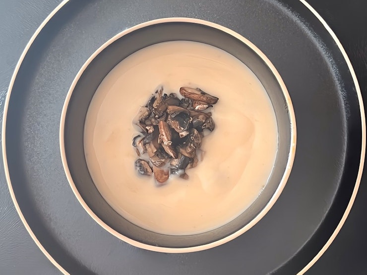 A bowl of French brie soup with sliced mushrooms on top with non-alcoholic brandy cream.